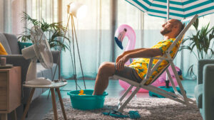 Mann, der die Sommerferien zu Hause verbringt und so tut, als sei er am Strand, er sonnt sich in seinem Wohnzimmer und ruht sich auf einem Liegestuhl aus