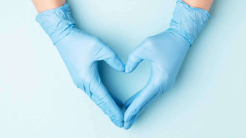 Hände eines Arztes in medizinischen Handschuhen in Form eines Herzens auf blauem Hintergrund