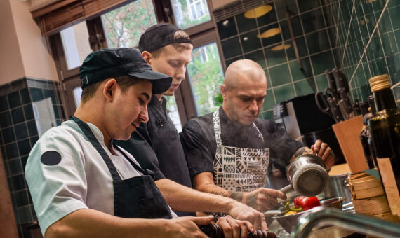 Teamarbeit. Küchenchef und seine beiden Assistentinnen in Schürzen kochen ein neues Gericht in einer modernen Küche, Kochvorgang