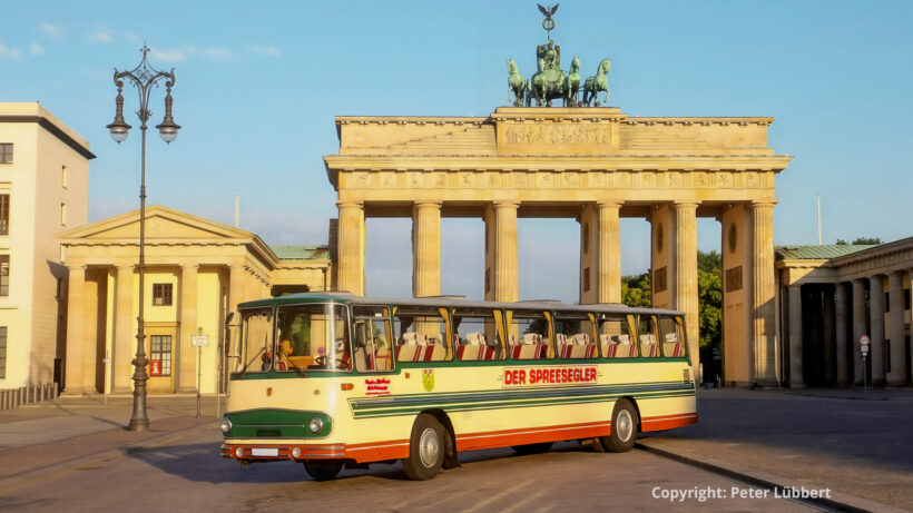 Oldtimerbus von 1972 steht vor dem Brandenburger Tor in Berlin in der Morgensonne bei blauem Himmerl