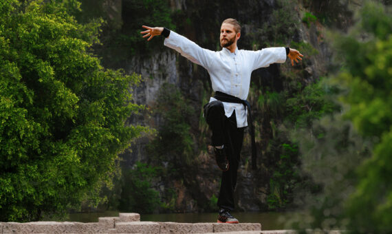 Mann Trainiert Tai Chi auf einem Felsen in der Natur und hebt dabei seine Arme bedeutungsvoll an