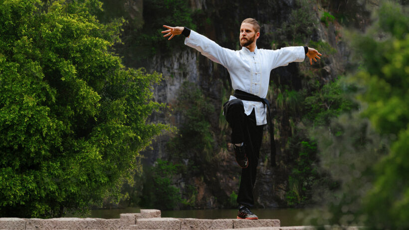 Mann Trainiert Tai Chi auf einem Felsen in der Natur und hebt dabei seine Arme bedeutungsvoll an