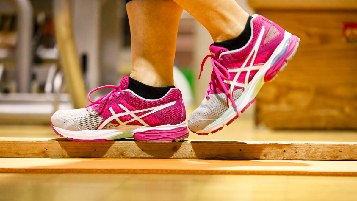 Balanceübung Beim Sport, zwei Füße mit Turnschuhen sind auf einem Holzbalken zu sehen