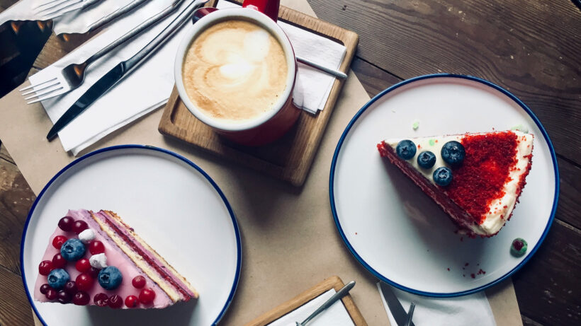 Kaffeetasse mit Milchschaum und zwei Stück Red Velvet-Kuchen angerichtet