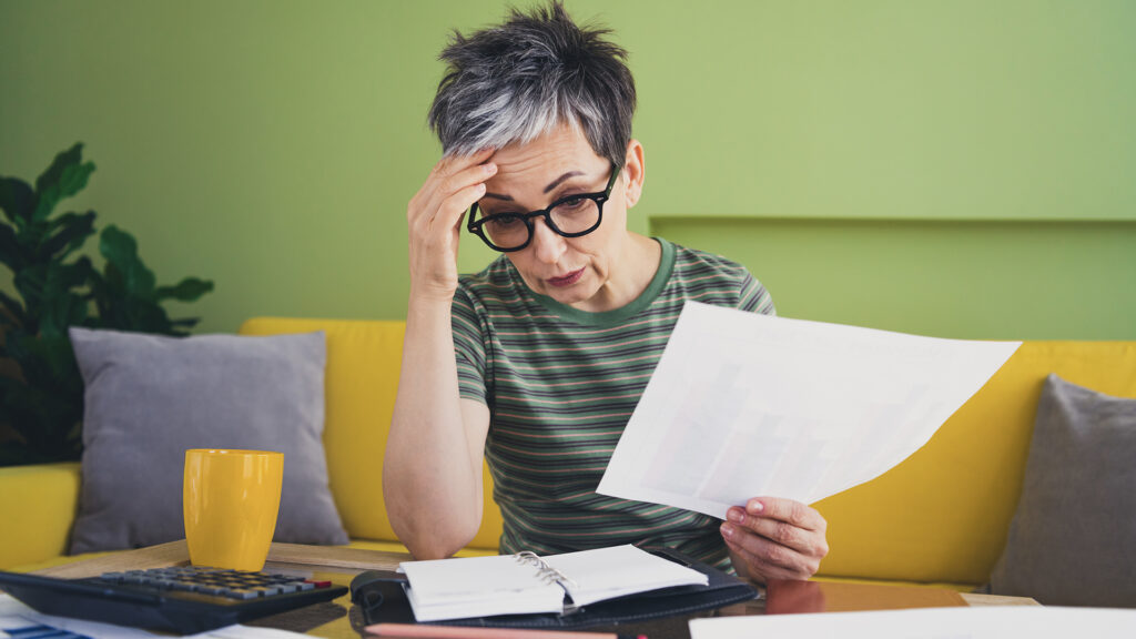 Foto einer charmanten Rentnerin, die verärgert und gestresst ist, mit Arbeitsunterlagen, grün gekleidet, Zimmer