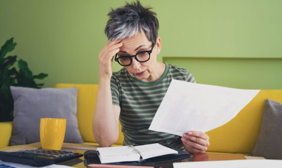 Foto einer charmanten Rentnerin, die verärgert und gestresst ist, mit Arbeitsunterlagen, grün gekleidet, Zimmer